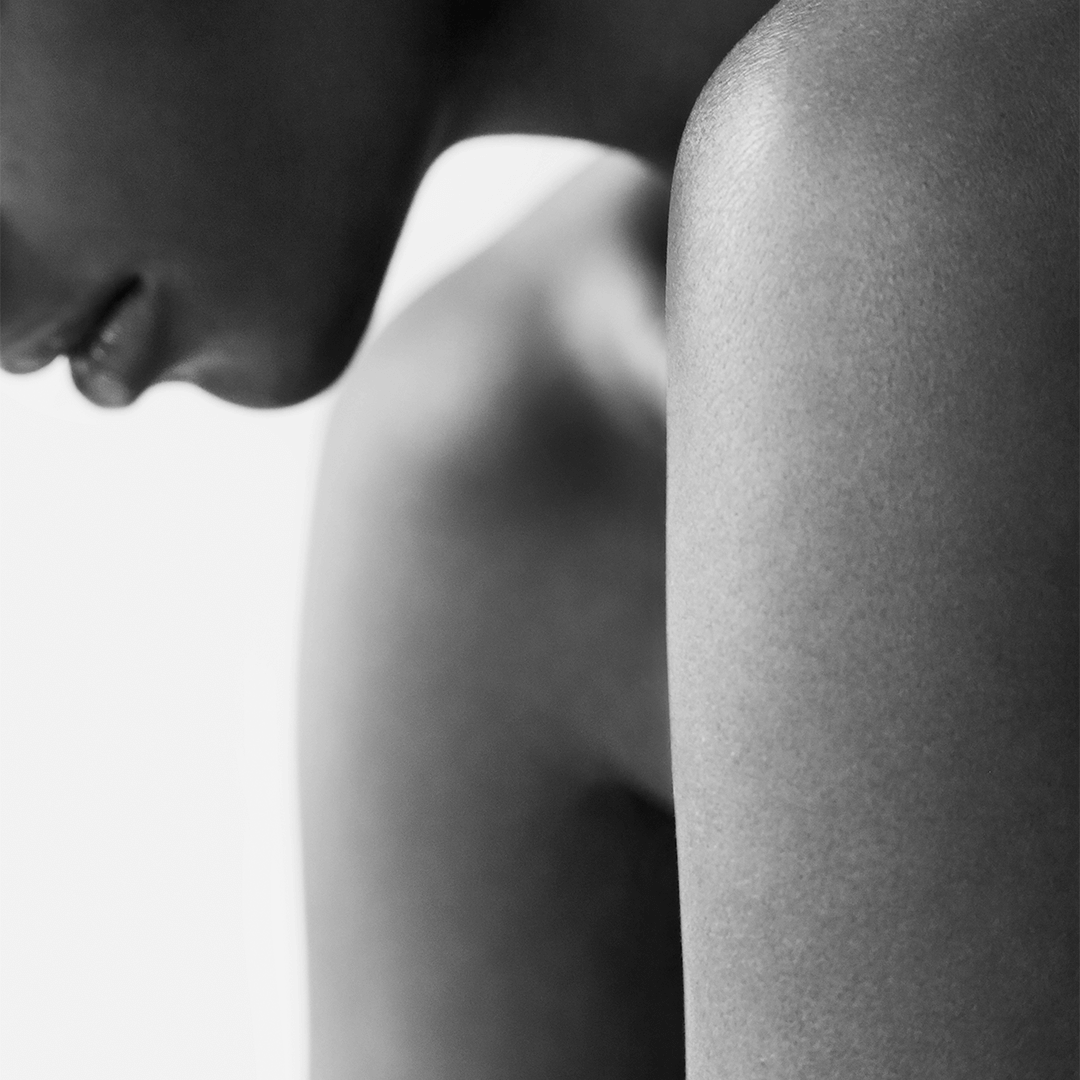 Close-up of a person's shoulder and neck, highlighting smooth skin and subtle contours in a black and white aesthetic.