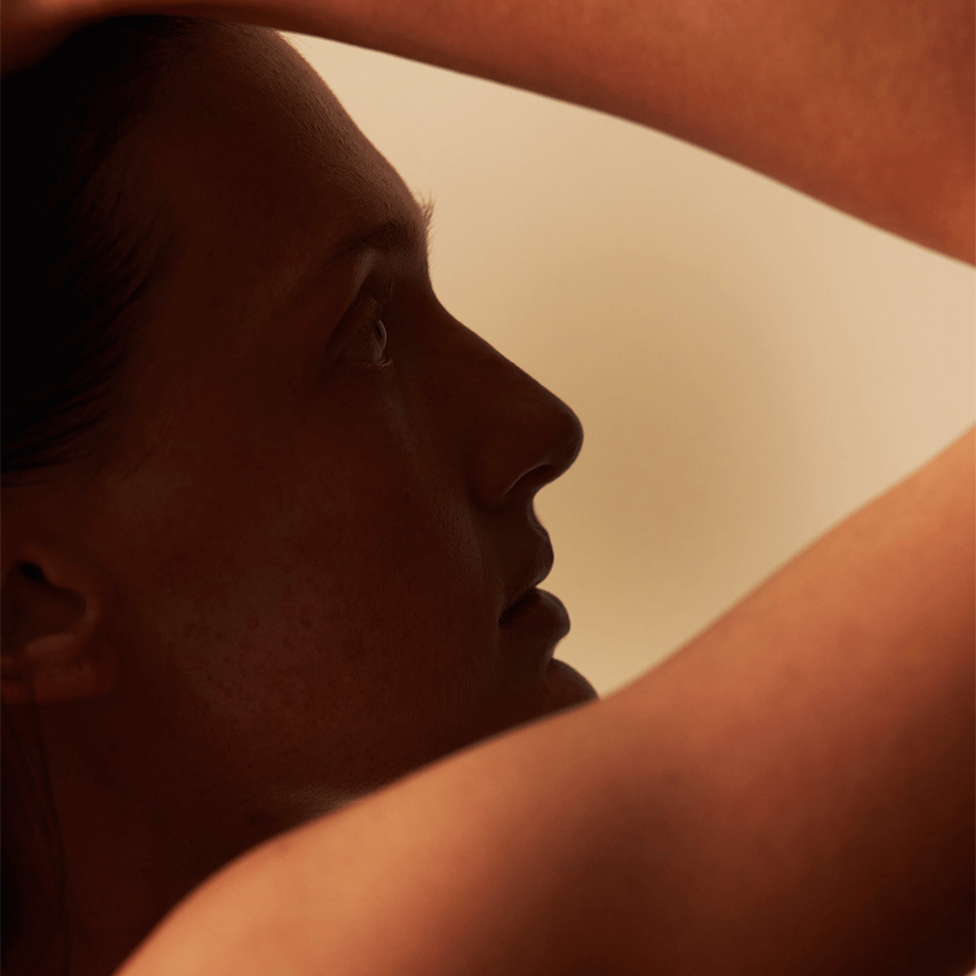 Side profile of a woman with hands behind her head, showcasing a serene expression and warm lighting.