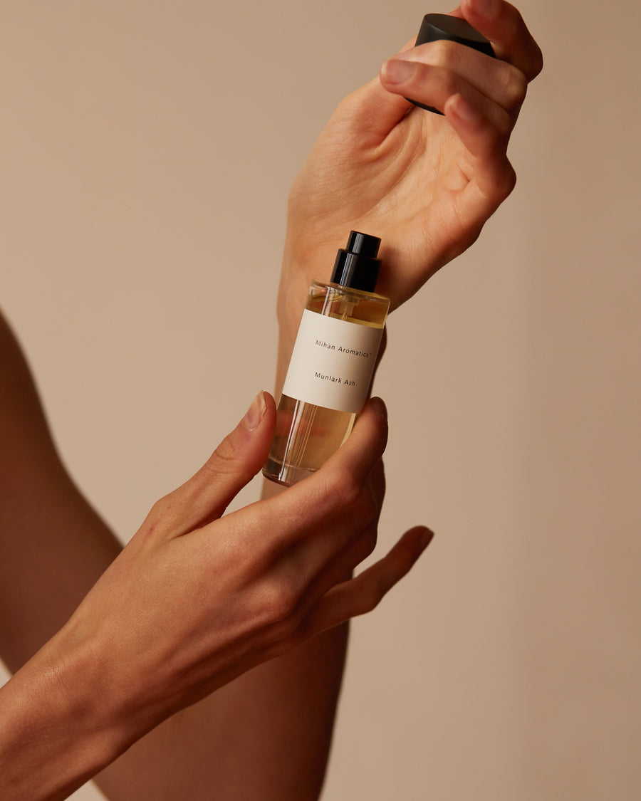 Hands holding Mihan Aromatics Munlark Ash parfum, spraying it onto the wrist