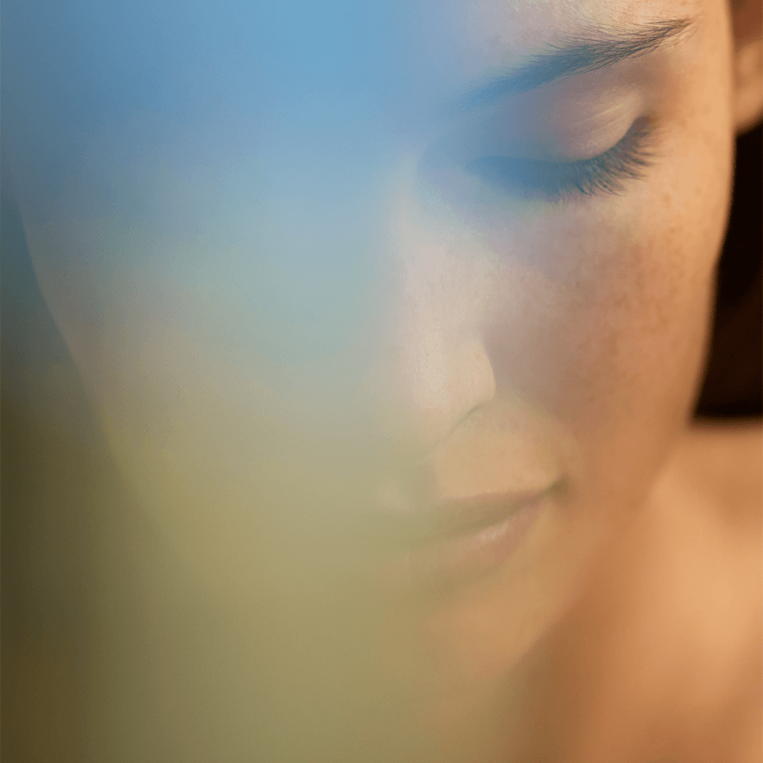 Close-up of a serene woman with closed eyes, showcasing calmness and tranquility in a soft, blurred background.