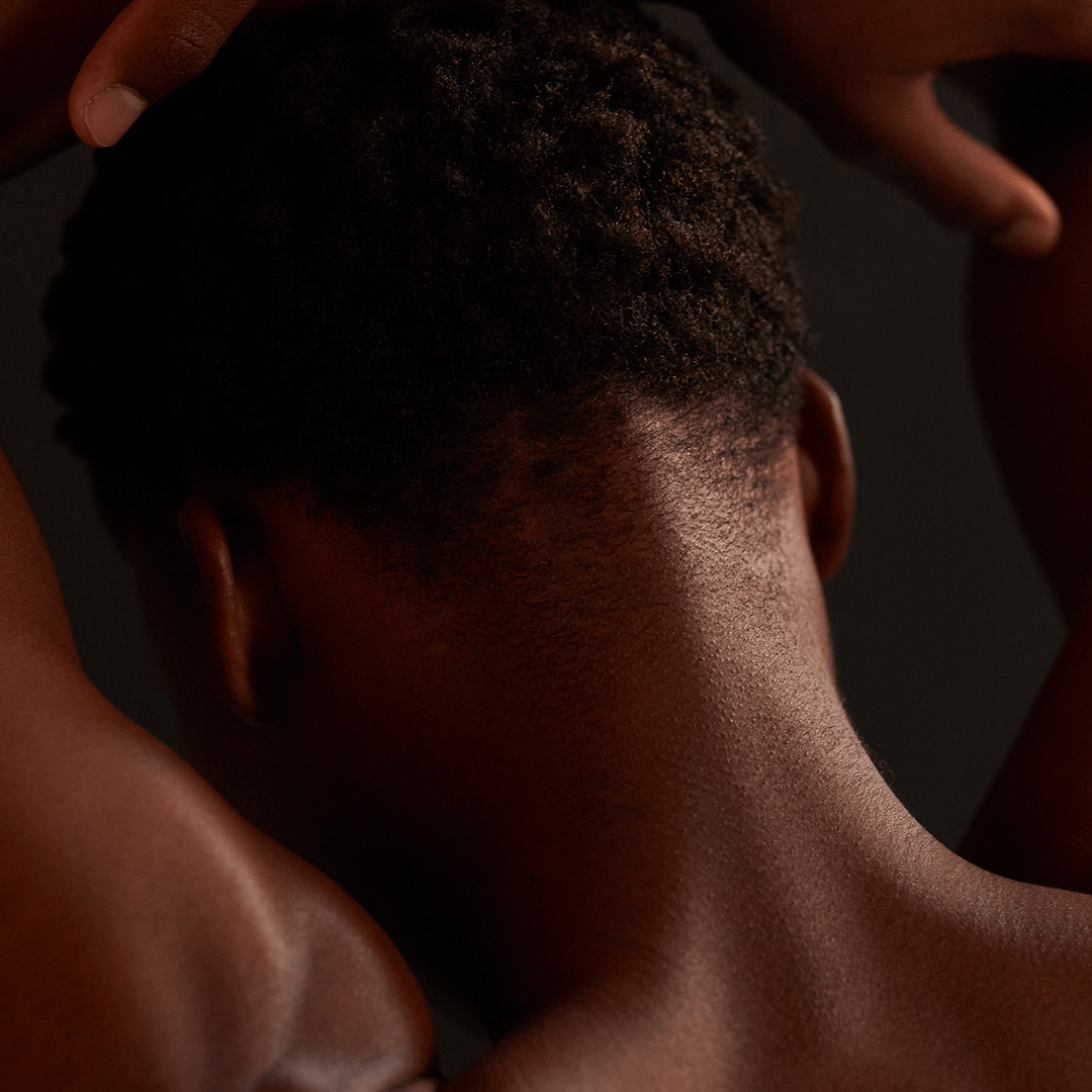 Close-up of a person's neck and shoulders, showcasing natural hair texture against a dark background.