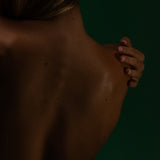 Bare back in warm shadow against deep green, a hand resting on the shoulder, Mihan Aromatics Series Three campaign