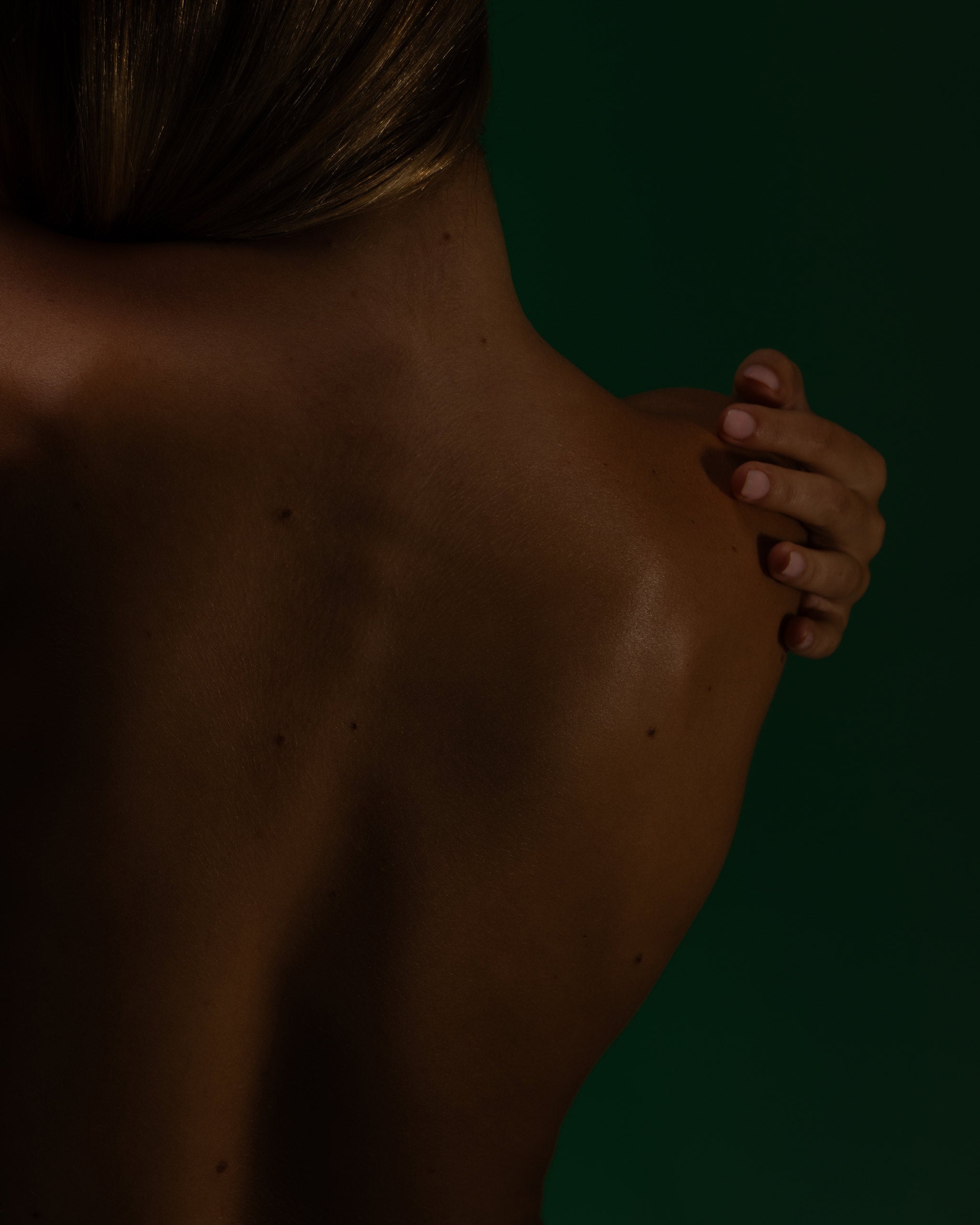 Bare back in warm shadow against deep green, a hand resting on the shoulder, Mihan Aromatics Series Three campaign
