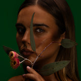 Model holding gum leaves and red gum blossom to her face against deep green, Mihan Aromatics Series Three campaign