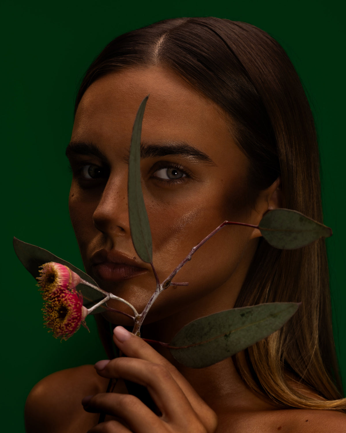 Model holding gum leaves and red gum blossom to her face against deep green, Mihan Aromatics Series Three campaign