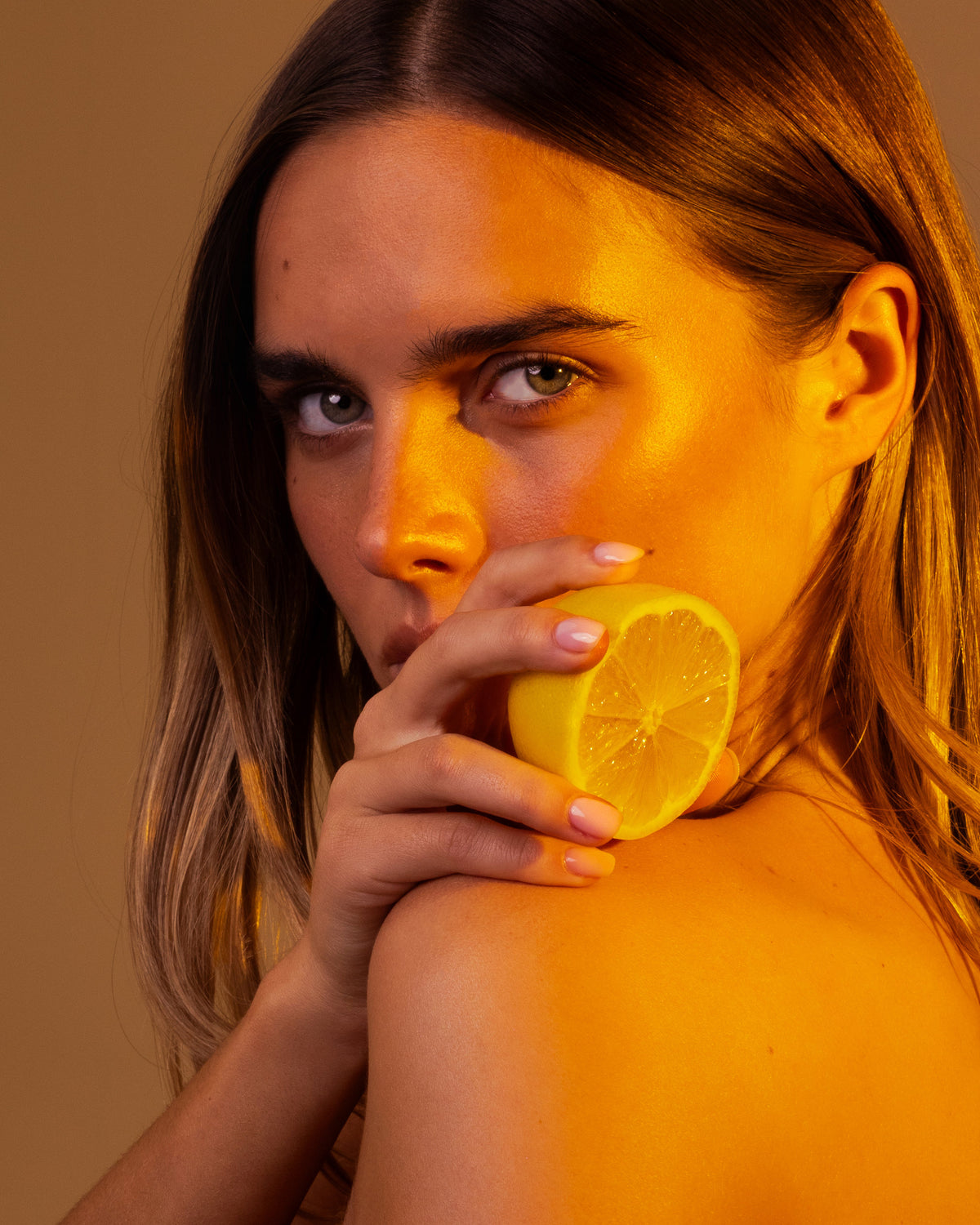 Model holding a cut lemon to her lips in amber light, Mihan Aromatics Series Three campaign