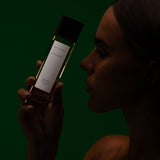 Model in shadow raising a Mihan Aromatics Eucalyptus Bloom parfum bottle to her face against deep green