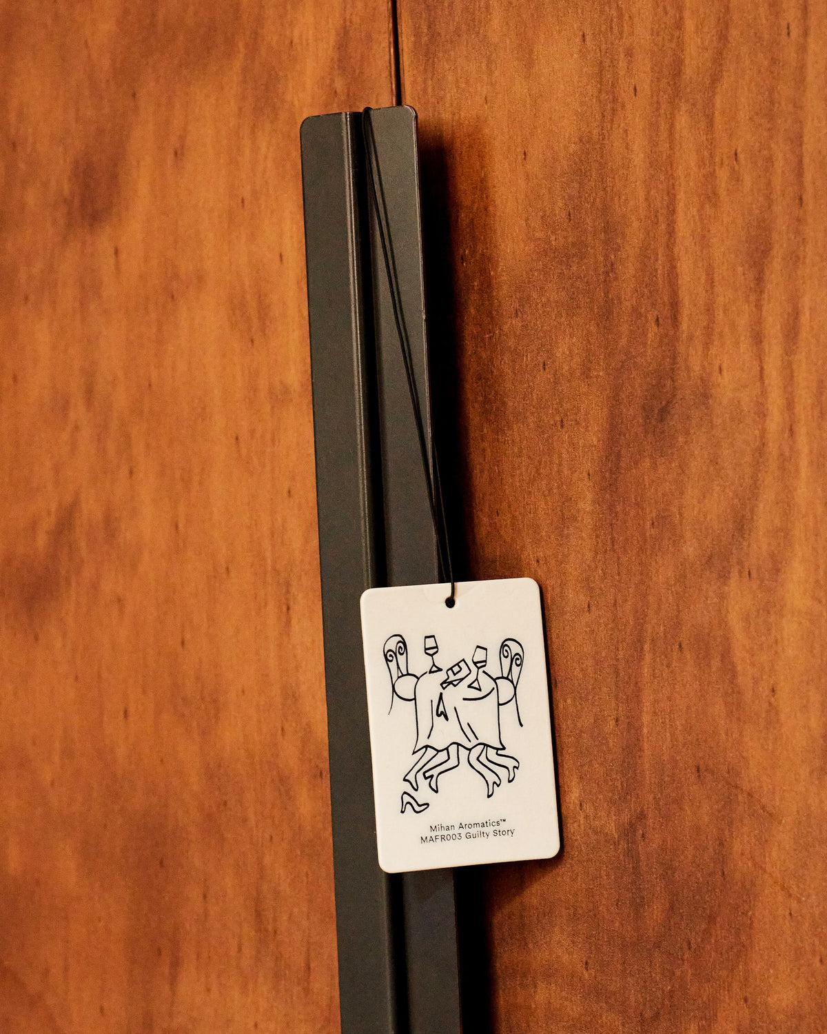 Mihan Aromatics Guilty Story Air Fragrance hanging from a black handle on a timber door