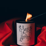 Mihan Aromatics Guilty Story candle being lit with a long match, nestled in red fabric