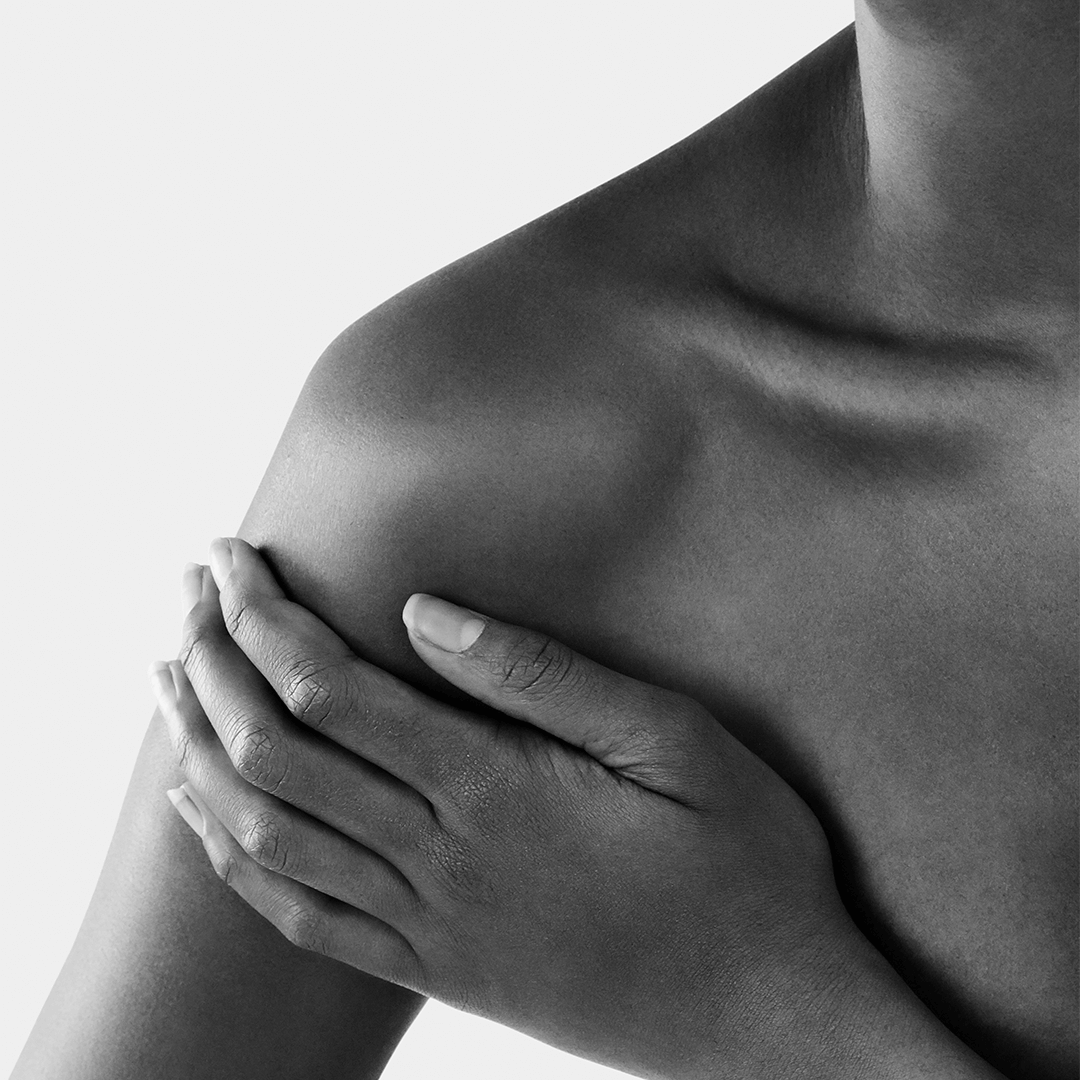 Close-up of a hand gently touching a bare shoulder, highlighting skin texture and soft features.