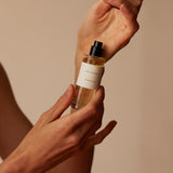 Hands holding Mihan Aromatics Munlark Ash parfum, spraying it onto the wrist