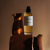 Mihan Aromatics Munlark Ash parfum bottle on draped earthen forms in warm amber light