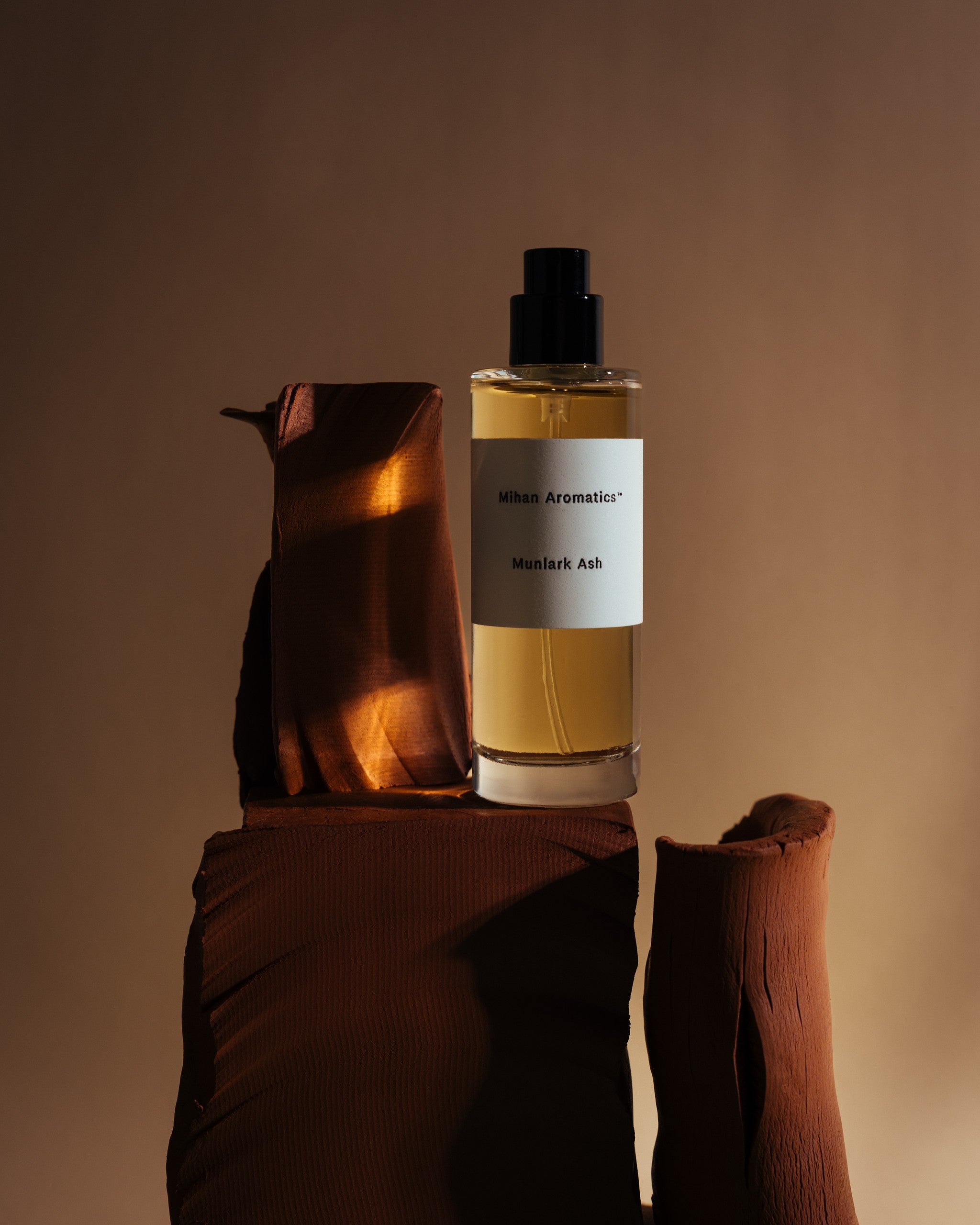 Mihan Aromatics Munlark Ash parfum bottle on draped earthen forms in warm amber light