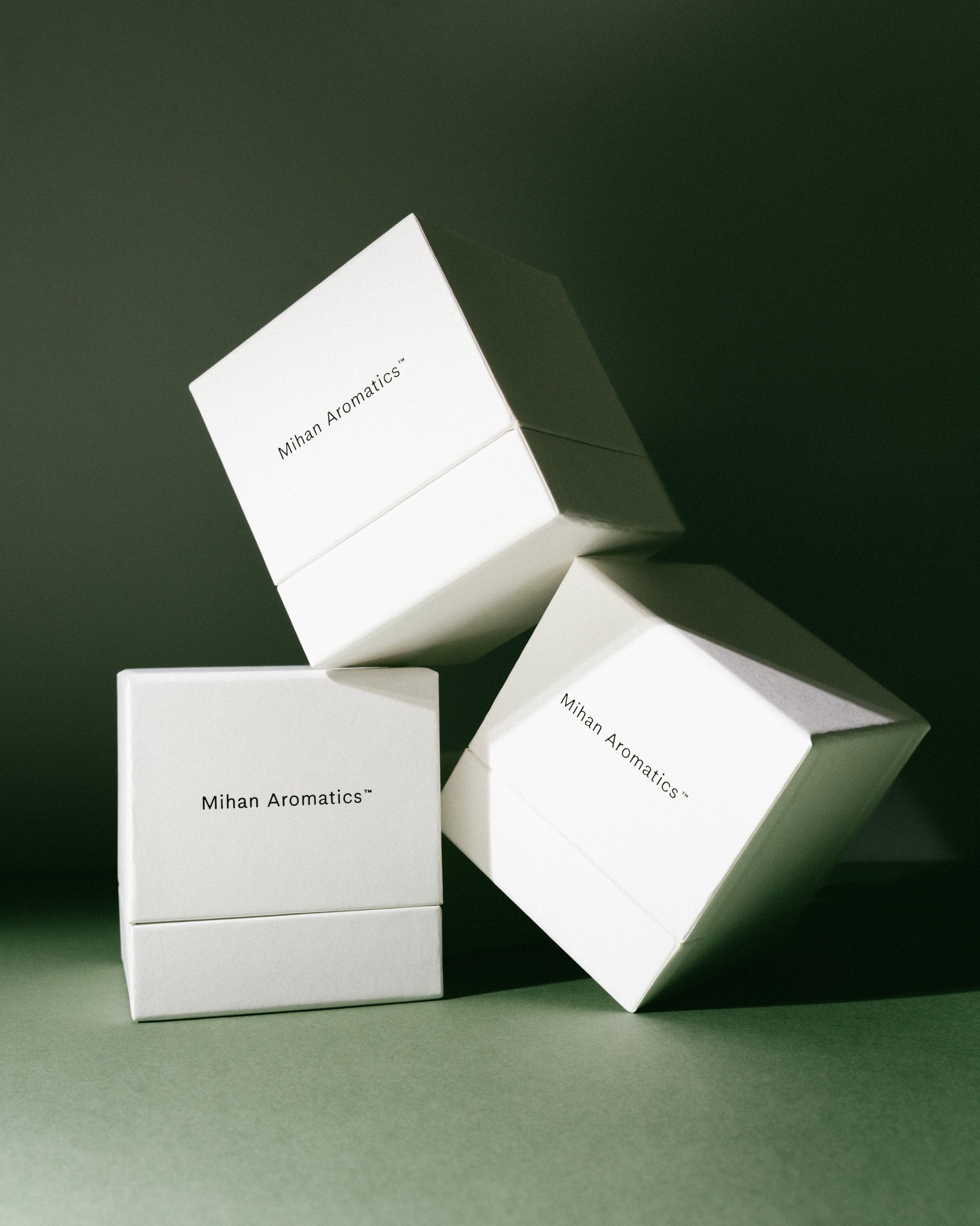 Stacked white Mihan Aromatics candle gift boxes on a deep green backdrop