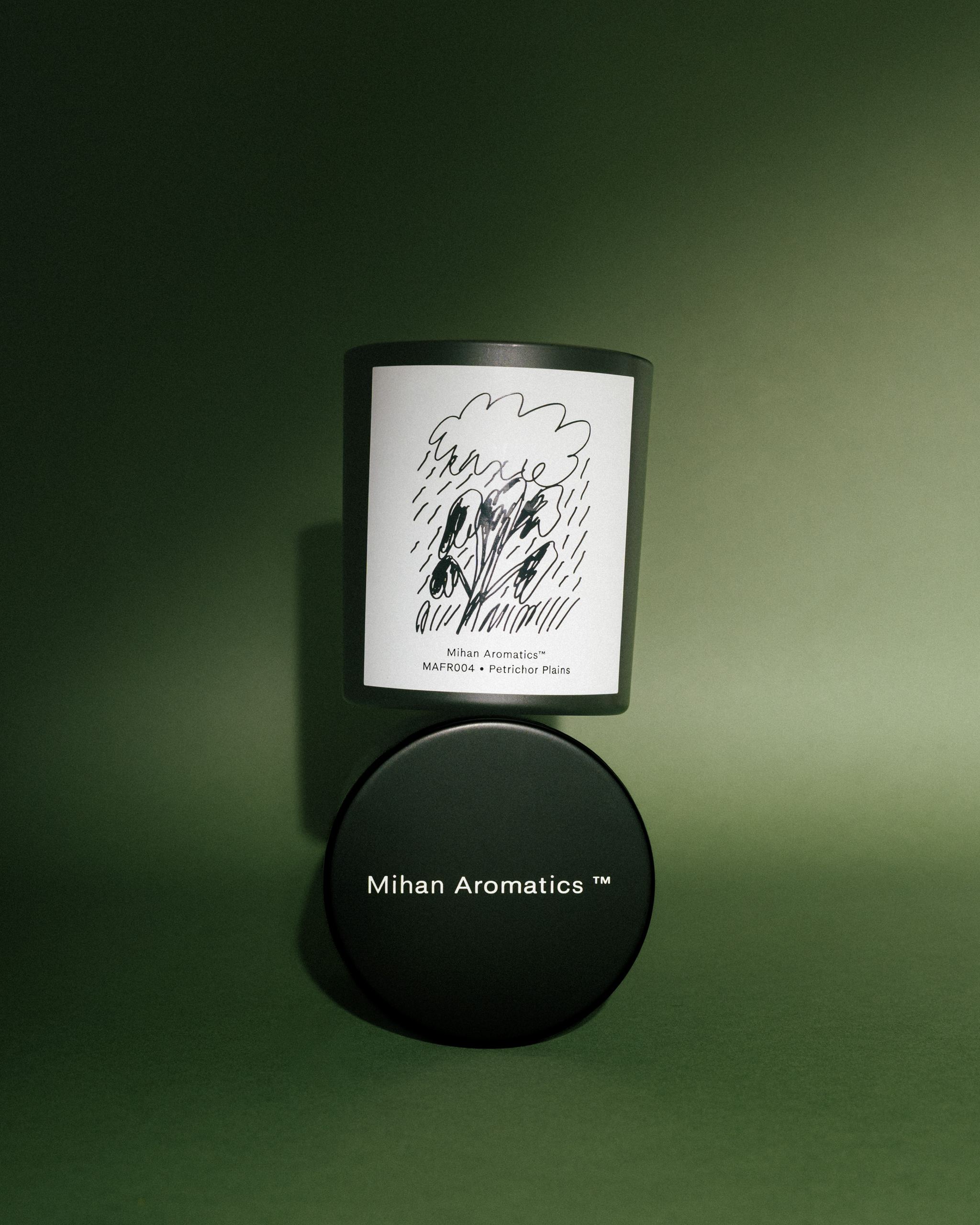 Mihan Aromatics Petrichor Plains candle resting on its black lid against a green backdrop
