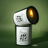 Two stacked Mihan Aromatics Petrichor Plains candles, the upper one lit and tilted with wax dripping