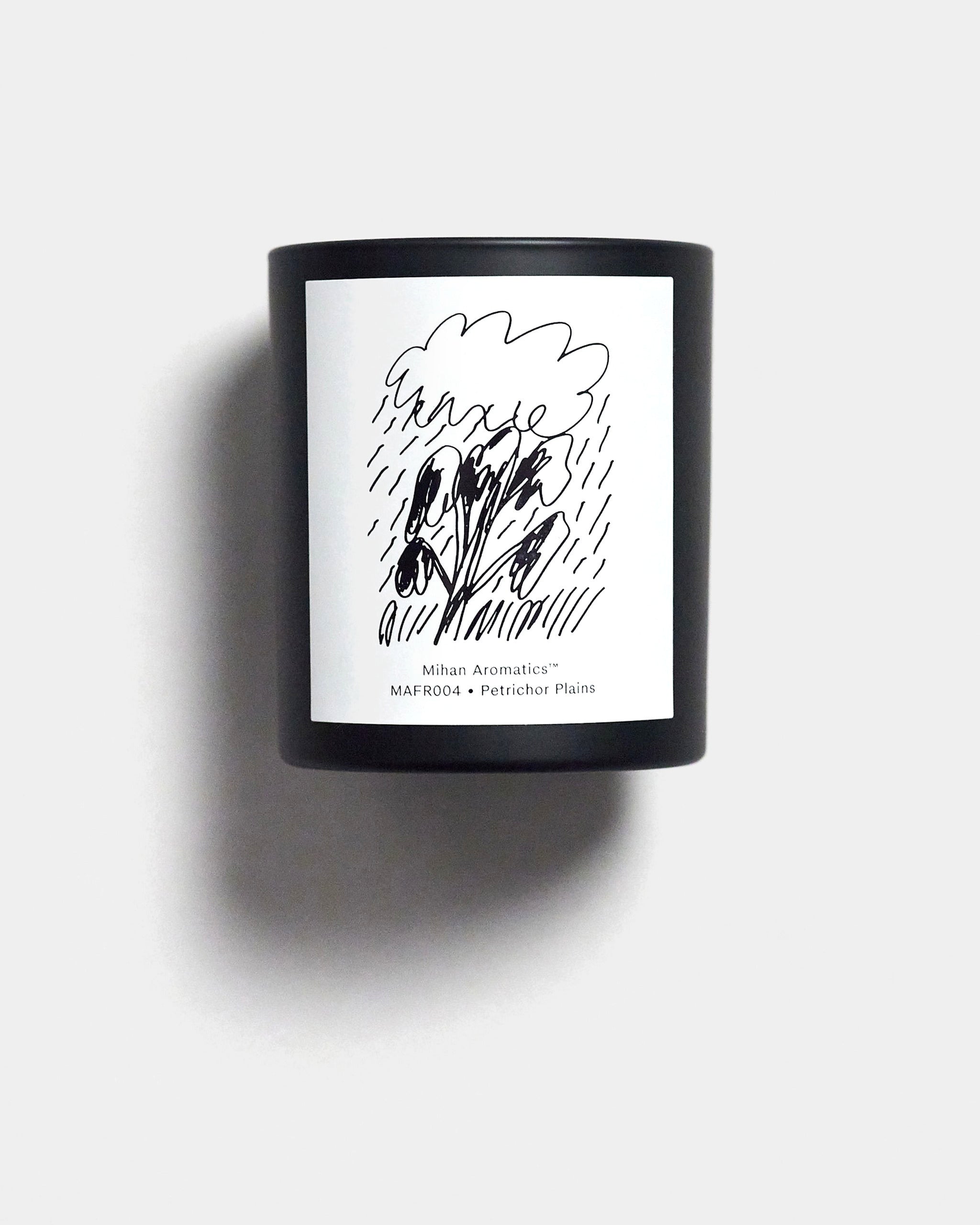 Mihan Aromatics Petrichor Plains candle in a black vessel with illustrated label on a Studio Grey backdrop