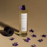 Mihan Aromatics Petrichor Plains parfum 100ml bottle uncapped among scattered violets on a warm sand backdrop