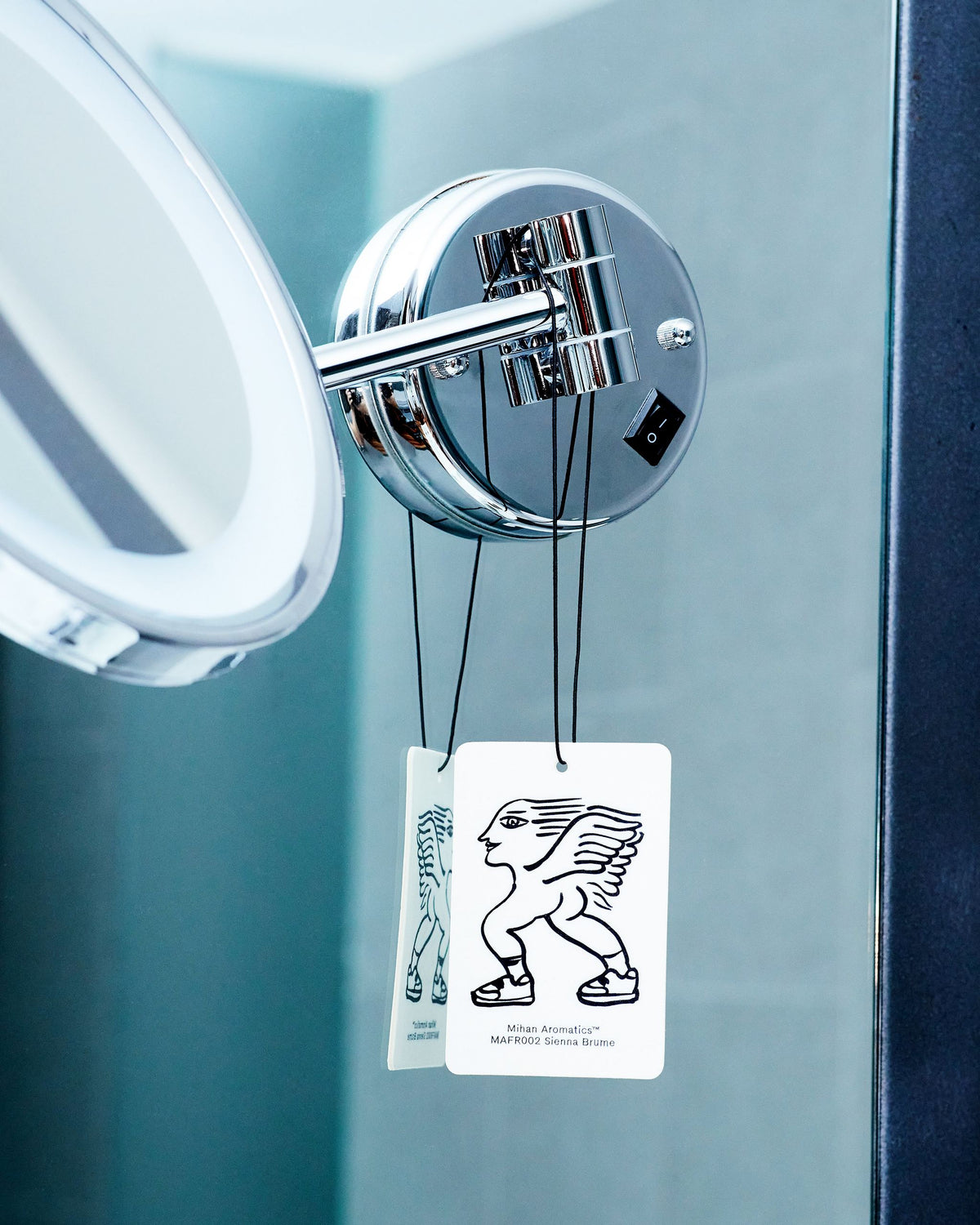 Two Mihan Aromatics Sienna Brume Air Fragrance cards hanging from a bathroom mirror arm