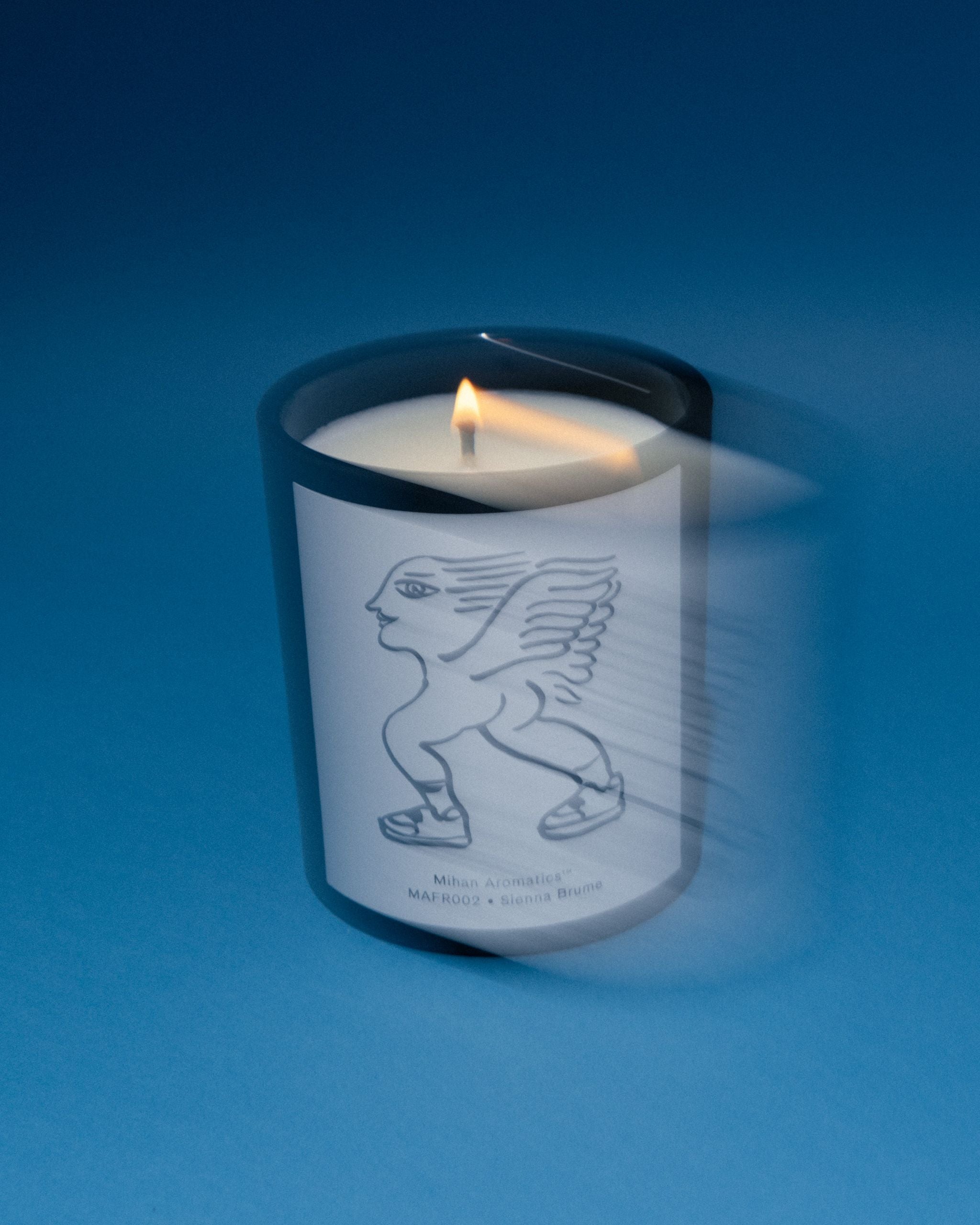 Lit Mihan Aromatics Sienna Brume candle with soft motion blur on a blue backdrop