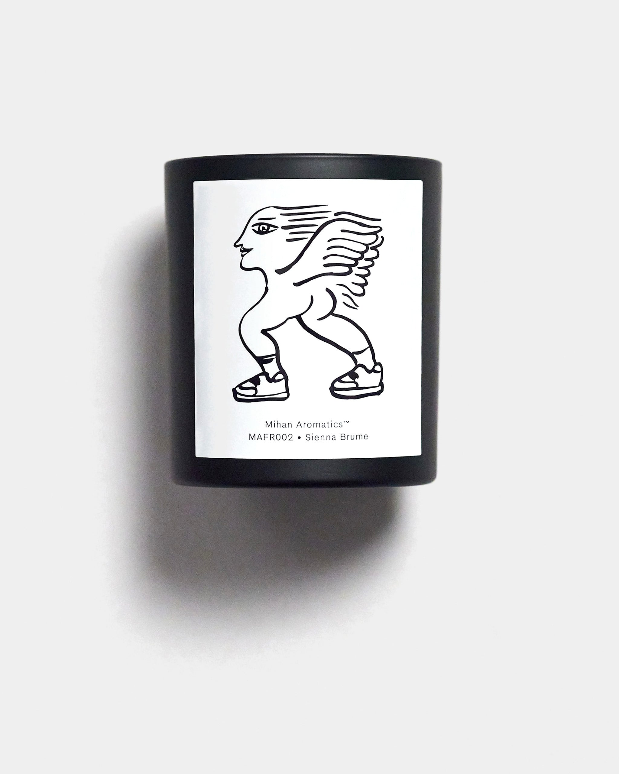 Mihan Aromatics Sienna Brume candle in a black vessel with illustrated label on a Studio Grey backdrop