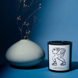 Mihan Aromatics Sienna Brume candle beside a ceramic vase of dried stems on a blue backdrop
