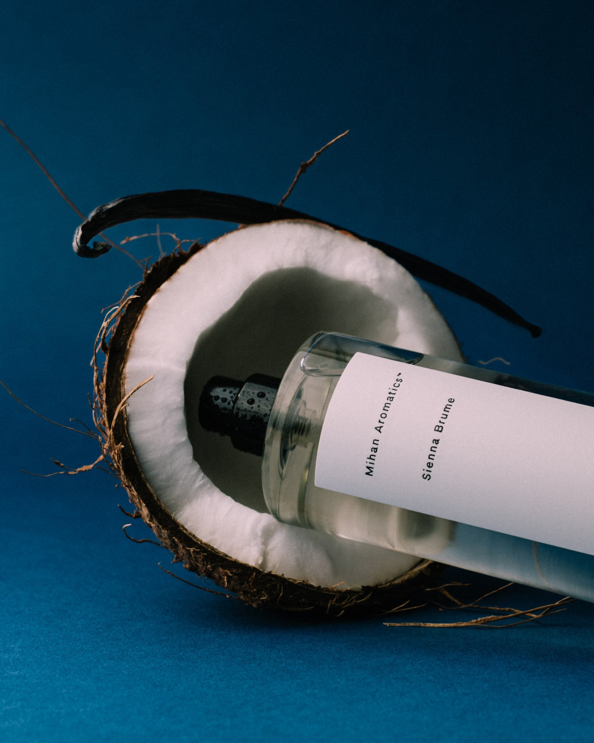 Mihan Aromatics Sienna Brume parfum bottle resting in a split coconut on a deep blue backdrop