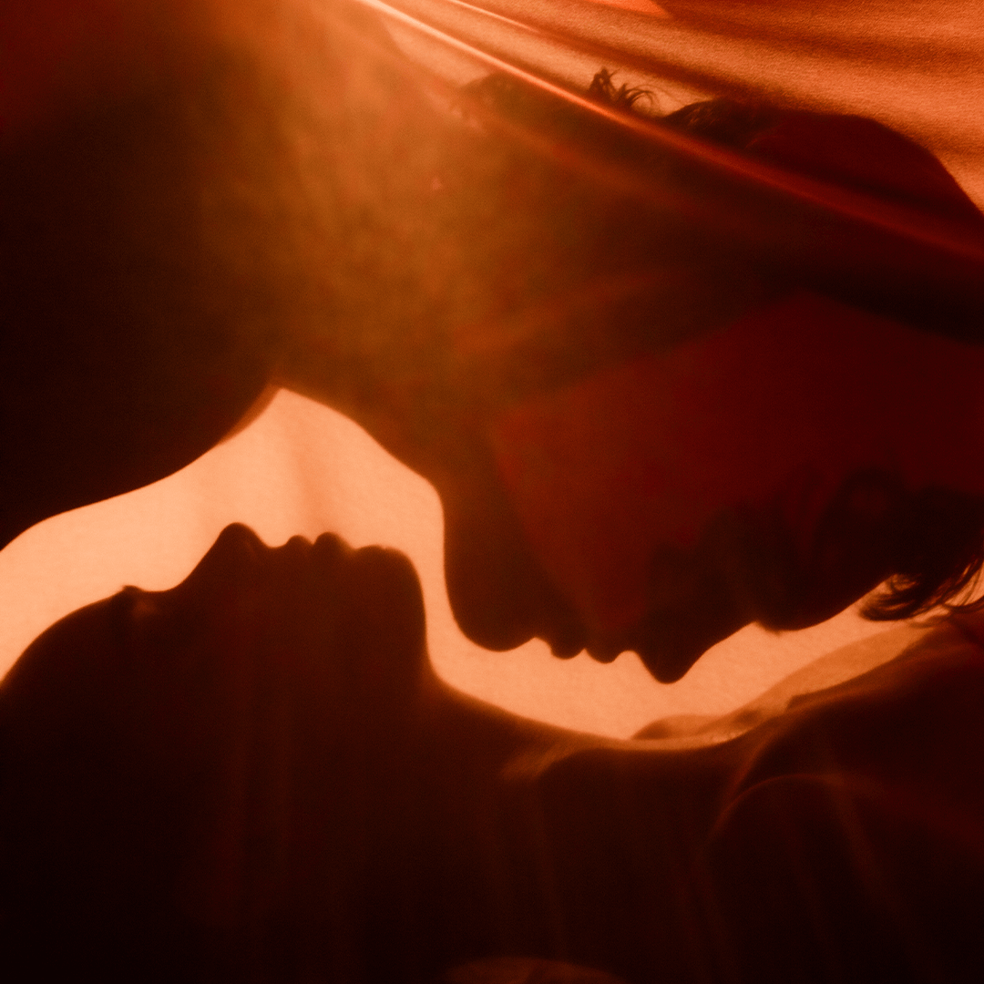 Silhouettes of a couple intimately close under warm light, captured in a romantic moment.