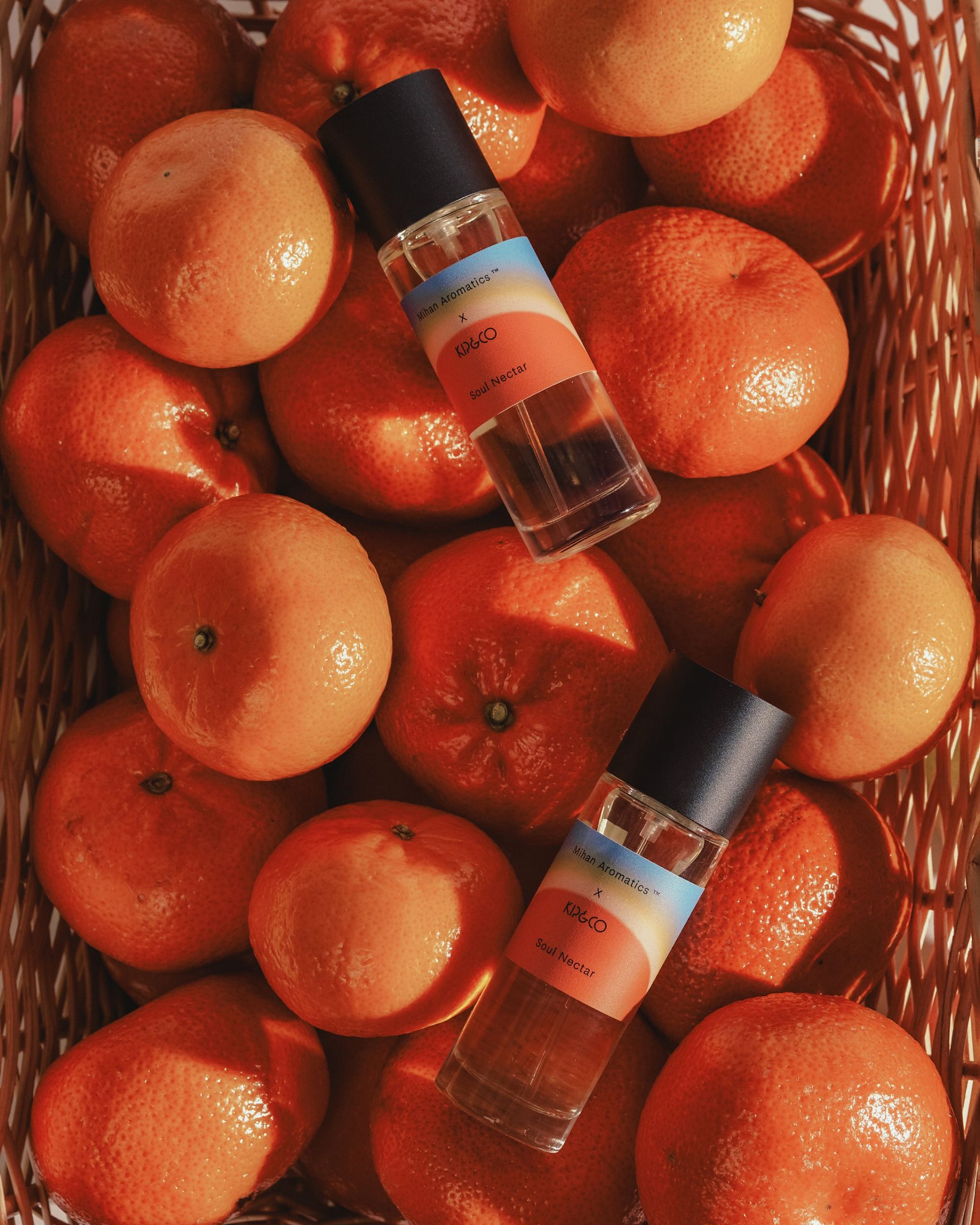 Two Mihan Aromatics x Kip&Co Soul Nectar parfum bottles resting in a basket of mandarins